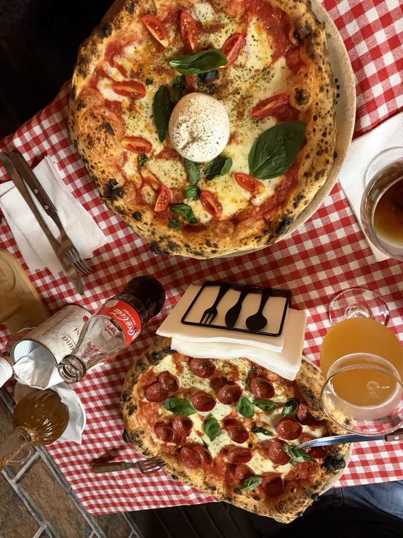 Two wood-fired pizzas from above, a burrata Margherita and a pepperoni, with drinks on a red-checked cloth